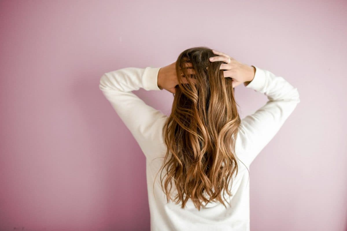 A woman running her hands through her hair against a soft pink wall